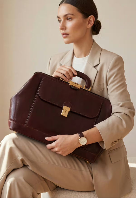 Bordeaux leather doctor’s bag resting on a woman’s lap with a light suit.