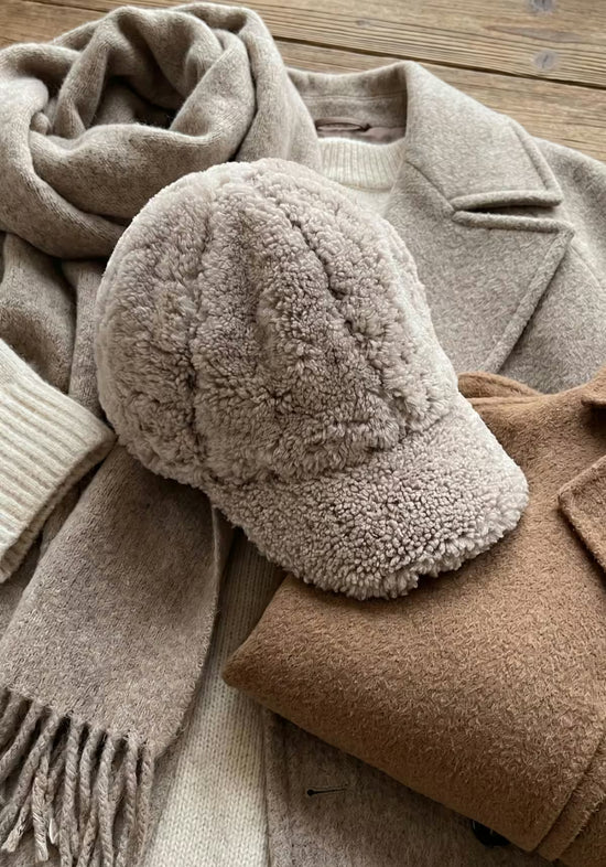 Camel sheepskin cap shown lying flat in detail, with a soft curly surface.