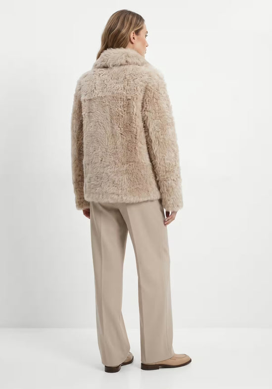 Rear view of the beige women’s curly sheepskin jacket with a straight cut.