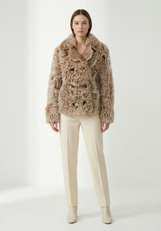 Women’s curly sheepskin jacket in cappuccino, shown frontally on a model with light trousers.