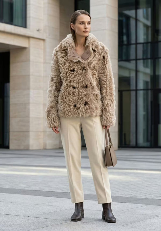 Women’s curly sheepskin jacket in cappuccino shown in a full styling look with trousers and boots.