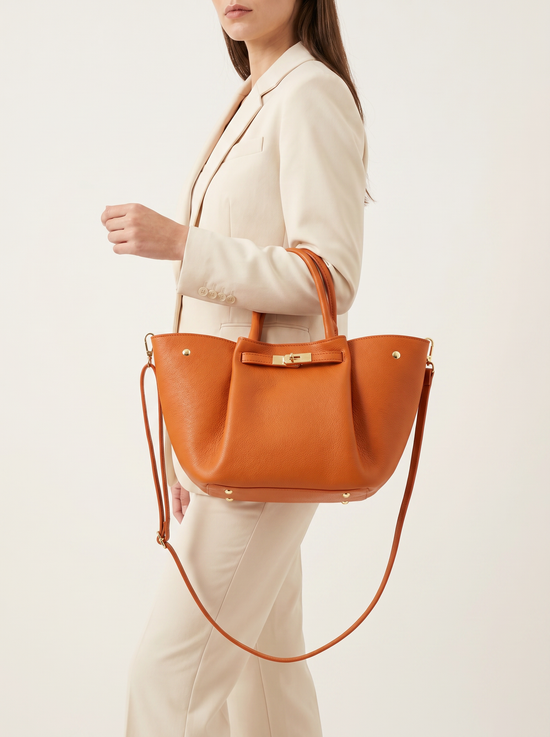Women's leather handbag in cognac worn on the model as a shoulder bag and by the top handles.