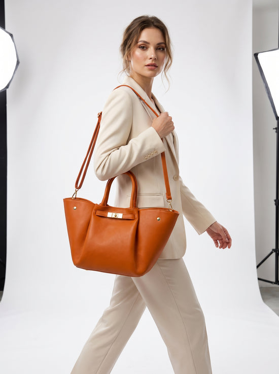 Women's leather handbag in cognac worn at the side, with the long strap and handles visible.