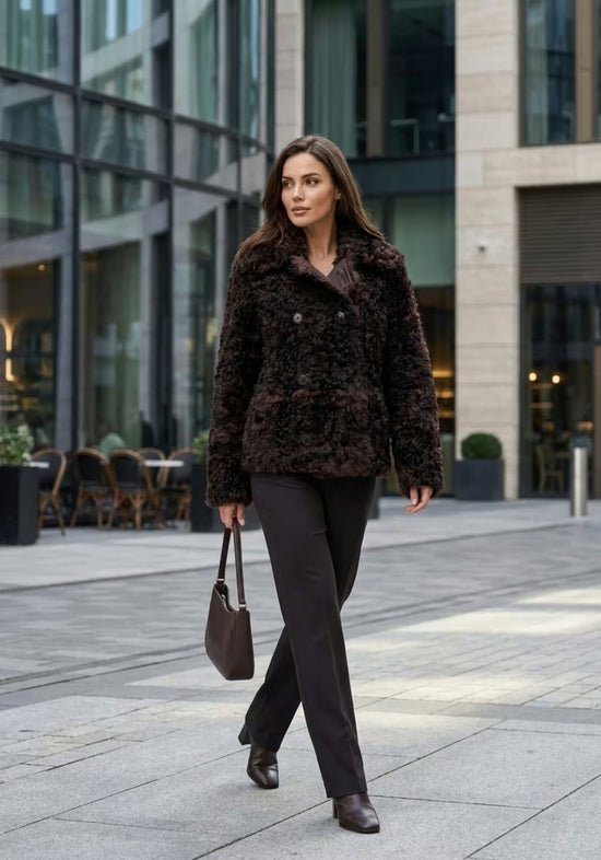 Women's curly sheepskin jacket in dark brown, worn front-on in a street-style look.