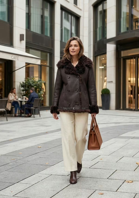 Women's reversible curly sheepskin jacket in dark brown, worn with the smooth side and fur collar.