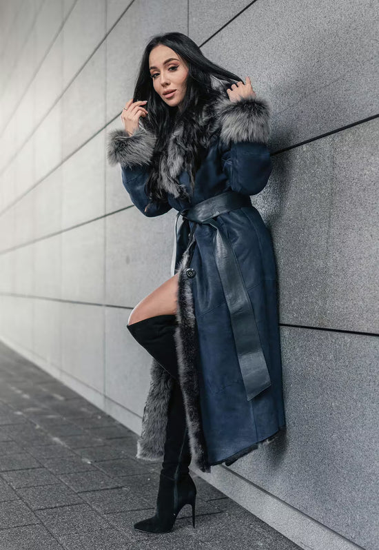 Women's sheepskin coat in dark blue, worn in side view against a wall with the hem open