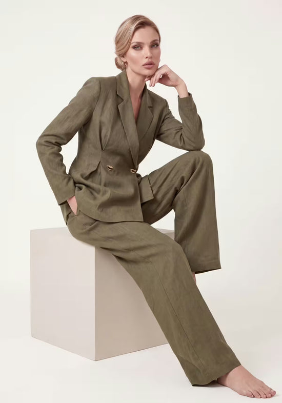 Women's linen suit in khaki, worn seated with blazer and wide palazzo trousers.