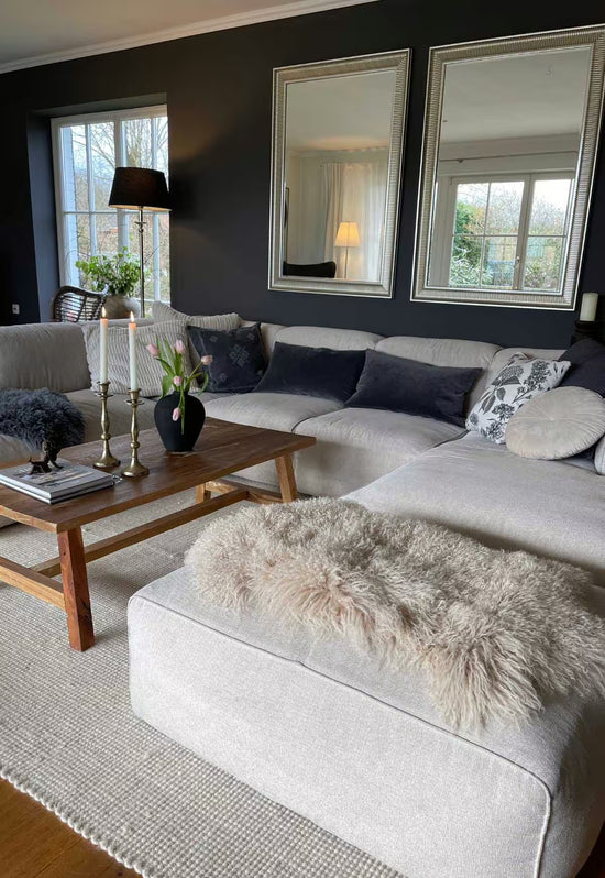 Beige sheepskin decorative rug on a light ottoman in front of a dark painted wall.