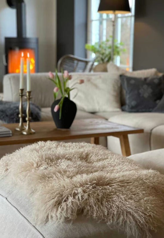 Beige sheepskin decorative rug on a sofa arm, showing the soft, curly pile in detail.