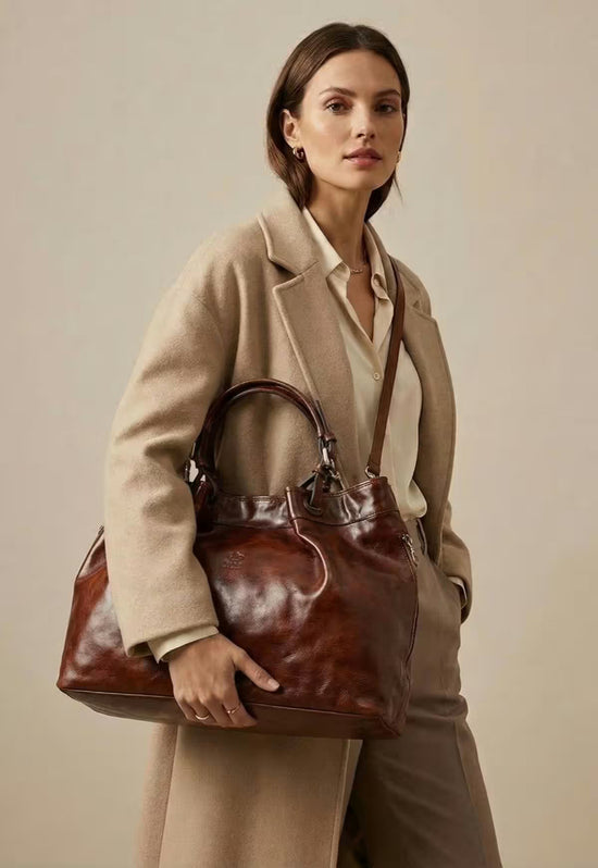 Brown leather handbag shown in a carrying view on a model wearing a light coat.