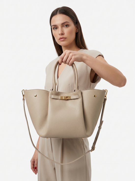 Women's leather handbag in cream beige, worn by a model with shoulder strap in the studio.