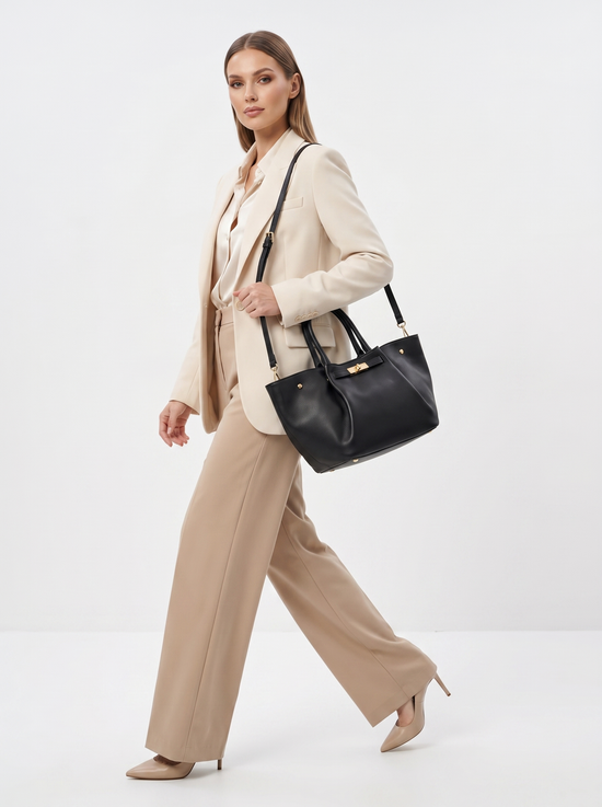 Black women’s leather handbag shown on a full-length model in a light trouser suit.