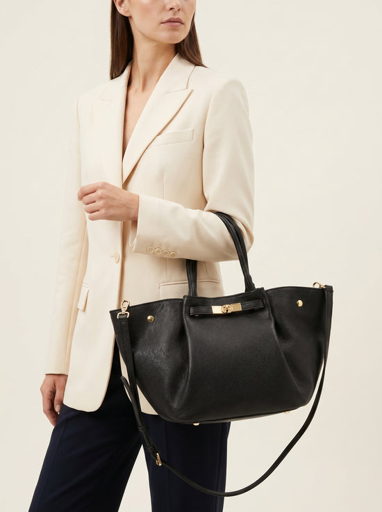 Black women’s leather handbag worn at the side with a light jacket.