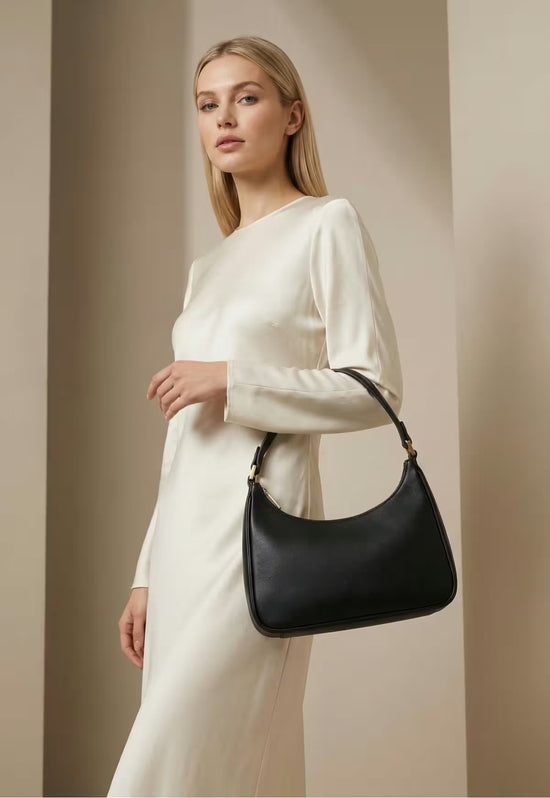 Black women’s leather handbag worn at the side with a light dress