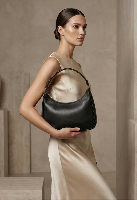 Black leather handbag for women shown as a worn model with a round handle