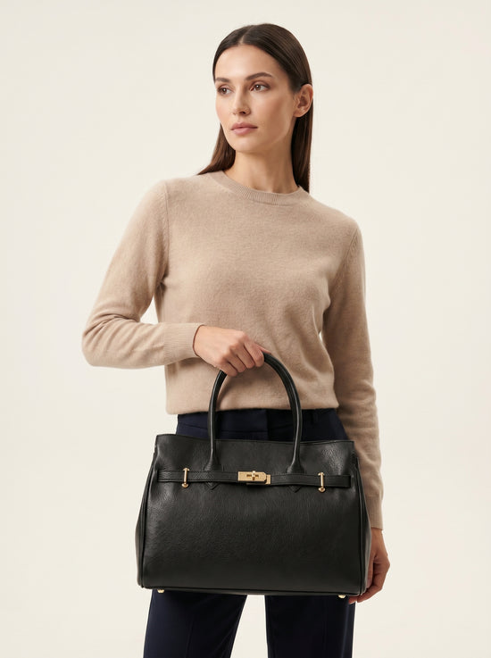 Black ladies' leather handbag, carried by hand in front of a beige jumper.