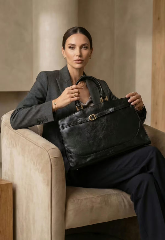 Black women's leather handbag worn by a woman while seated in an armchair