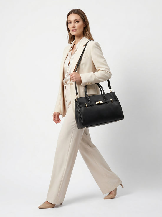 Black ladies' leather handbag in an angled view, worn with a light trouser suit.