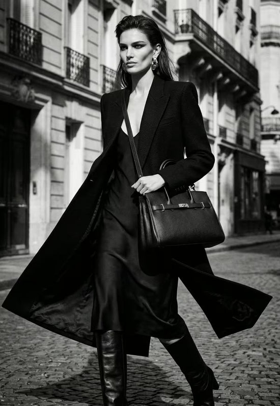 Black ladies' leather handbag worn in a black-and-white photo with a long coat.