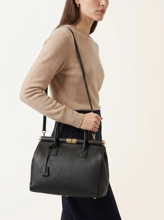 Black ladies' leather handbag shown at the side on a woman with long shoulder strap