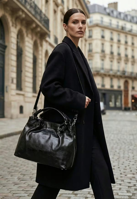 Black leather handbag with short handle and long strap, shown from the side while worn.