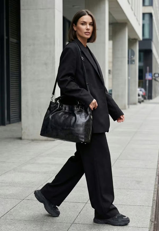 Black leather handbag with shoulder strap, carried by a woman in an urban setting.