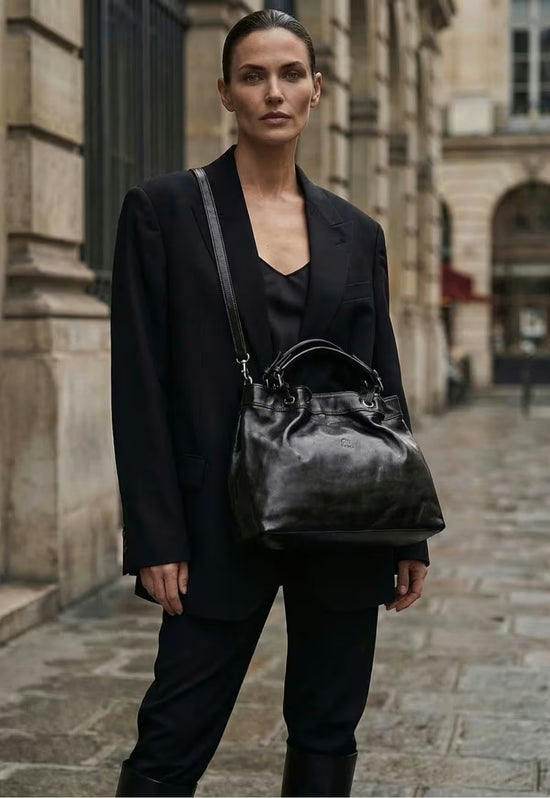 Women’s black leather handbag with shoulder strap, worn on a cobbled street.