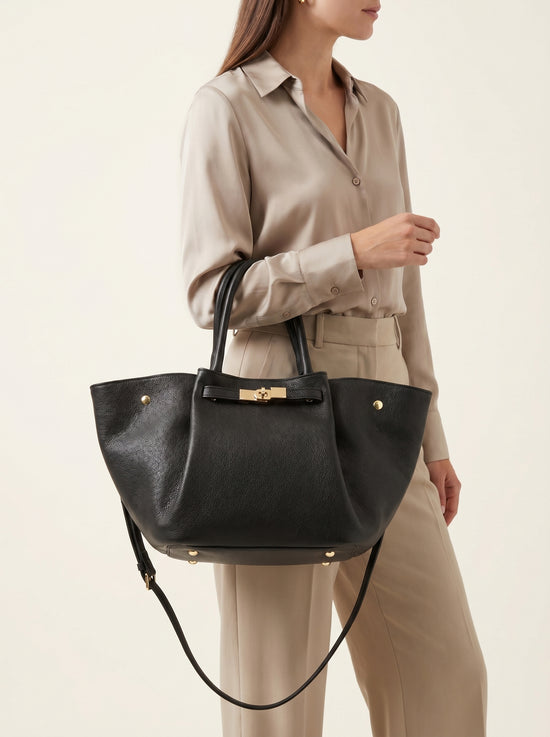 Black women’s leather handbag worn crossbody with a beige outfit.