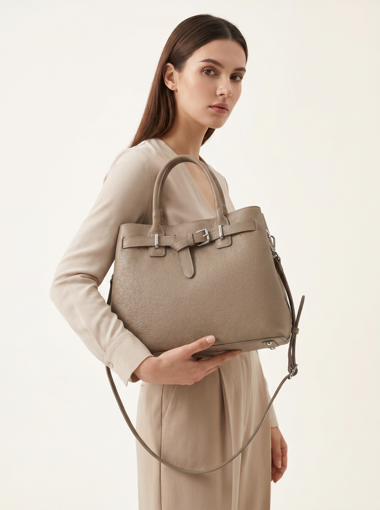 Taupe leather women’s handbag carried on the arm and shown with the shoulder strap.