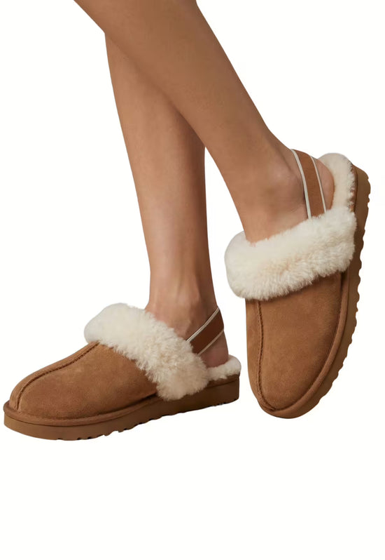 Brown women's sheepskin slippers worn on slim legs, isolated on a white background.