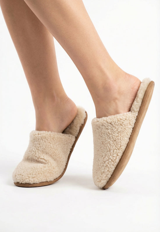 Women's sheepskin slippers in natural tone, worn on the feet in a side profile view