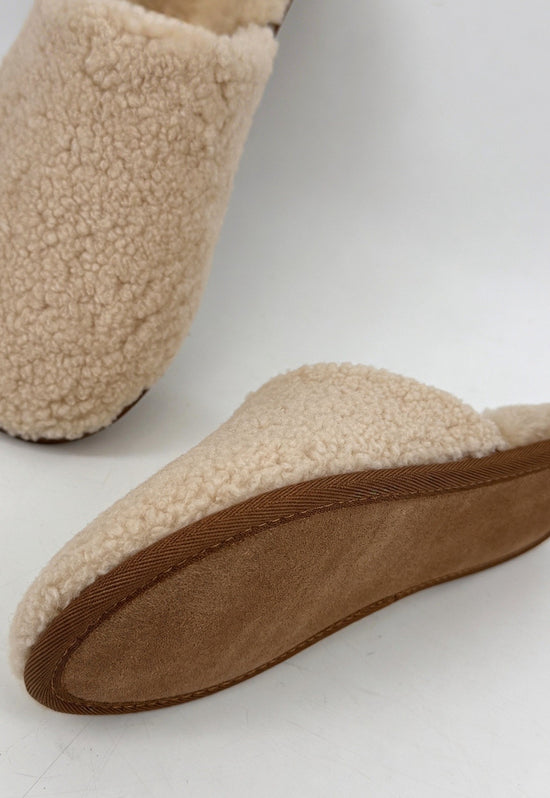 Women's sheepskin slipper in natural tone with a visible brown sole and curly upper