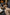 Brown women's sheepskin slippers seen on a relaxed person in a living room with a fireplace.