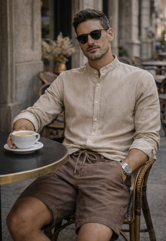Men’s linen shirt in beige, worn in a café with sunglasses and an open collar area.