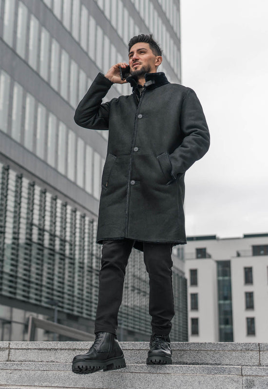 Worn black men's sheepskin street shoes shown in a full-body view with a long coat