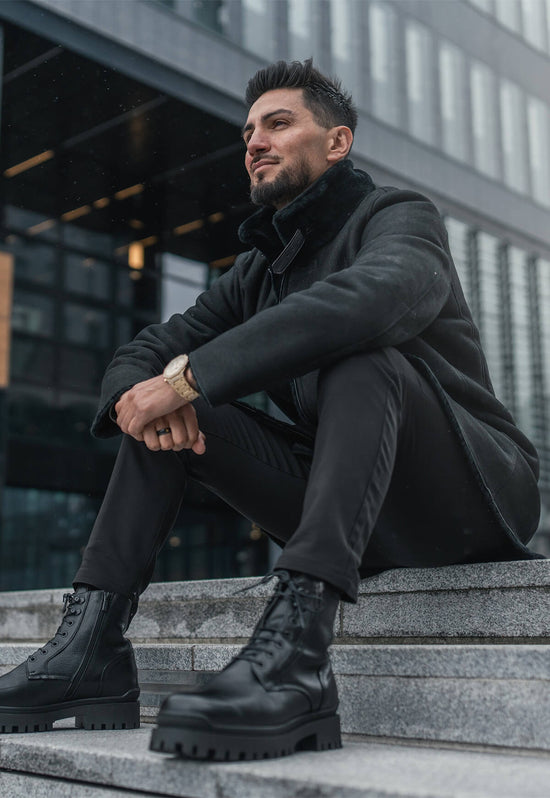 Worn black men's sheepskin street shoes with a coat in an outdoor city view