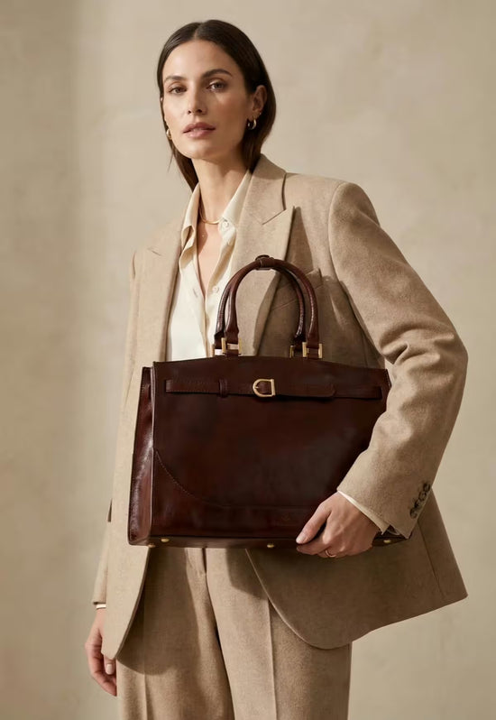 Brown leather hobo bag is worn by a woman as a shoulder bag with a beige suit.