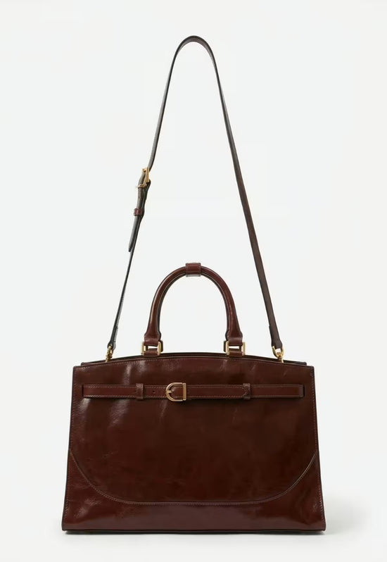 Brown leather hobo bag with a long shoulder strap and two handles on a light background.