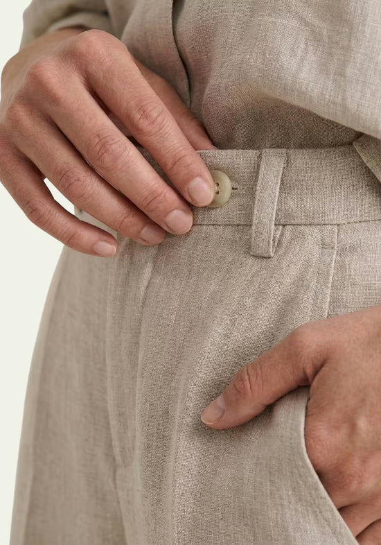 Detail of the beige women's linen trousers with button, belt loops and waistband.
