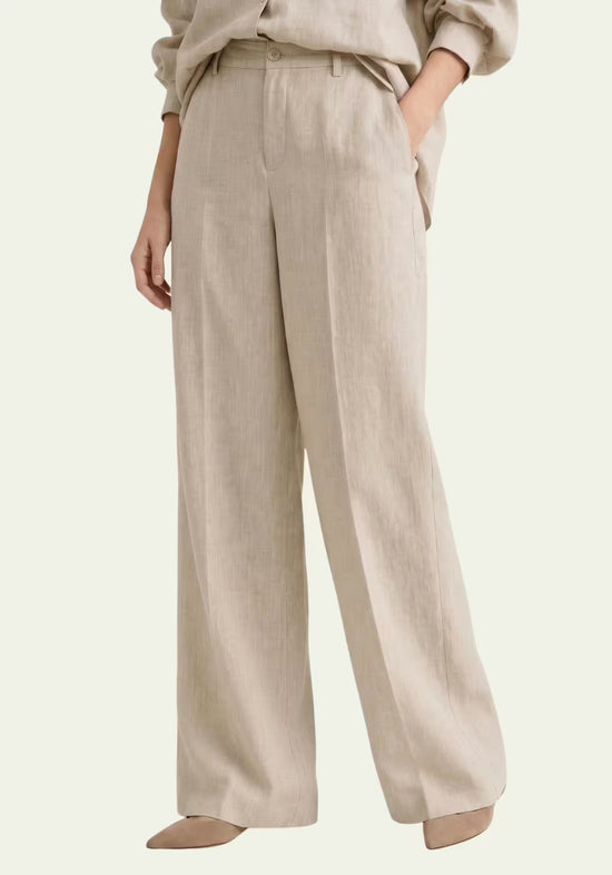 Beige women's linen trousers shown worn, with a wide cut and flowing drape.
