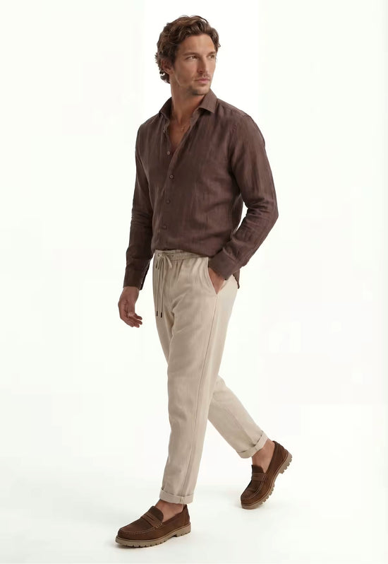 Men's beige linen trousers worn on a model in side view, with the turned-up hem visible.