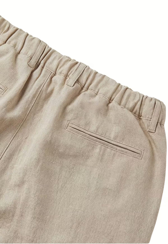 Detail of the beige linen trousers: elastic waistband, belt loops and a back pocket in the fabric.