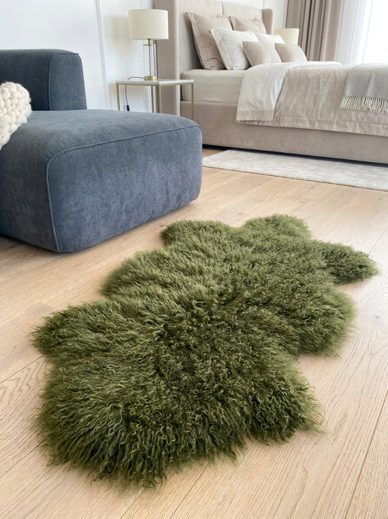 Green sheepskin lies spread out on a light wooden floor beside a bed and armchair.