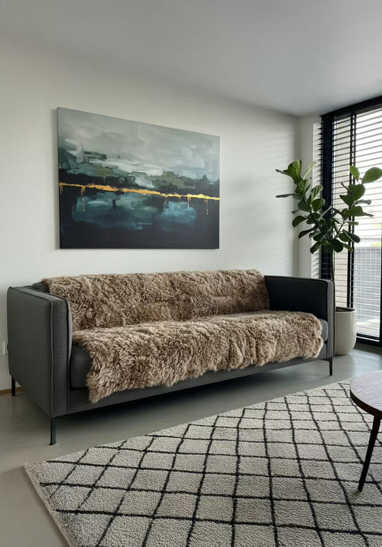Cappuccino sheepskin blanket made from curly sheepskin draped over a dark sofa.