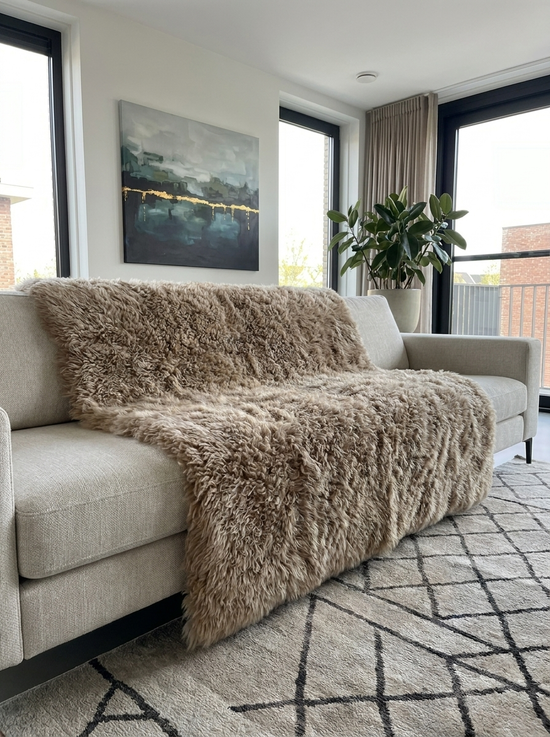 Sheepskin blanket made from curly sheepskin in cappuccino used as a throw on a light sofa.
