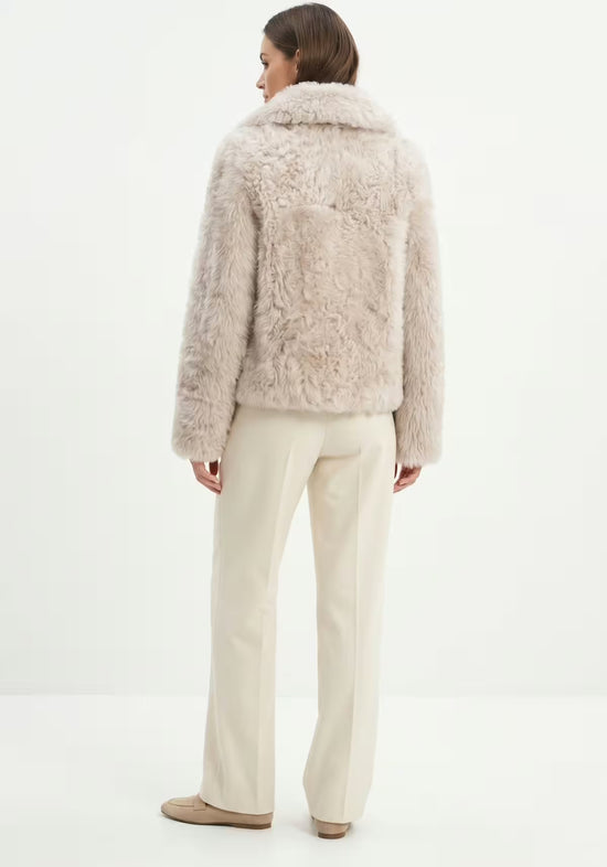 Women’s curly sheepskin jacket in cream beige, worn on a model from the back.