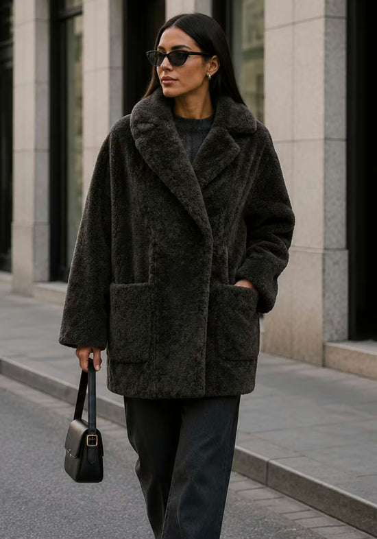 Women’s sheepskin jacket in khaki in an urban setting, worn front-on with pockets and wide lapels.