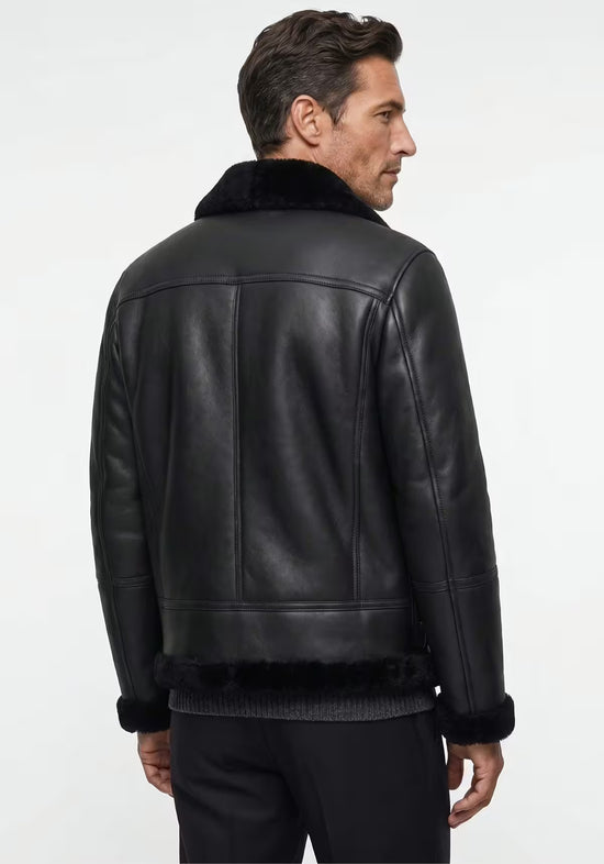 Black men's sheepskin jacket worn on the model from the back, with a smooth back panel and shearling hem.