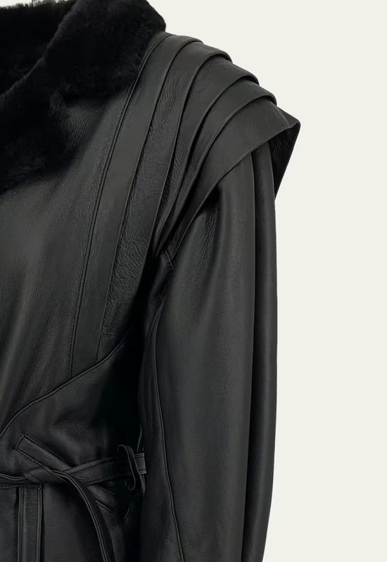 Close-up of the black sheepskin jacket showing the shoulder panel, sleeve and belt detail.
