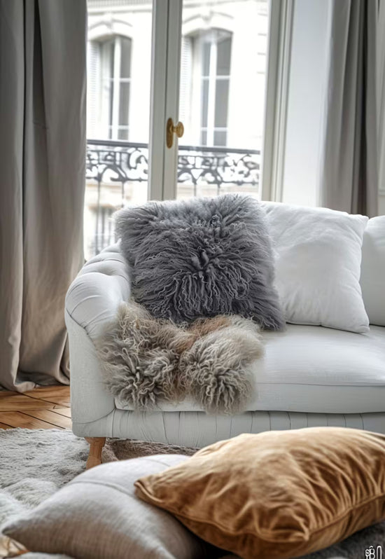 Grey sheepskin cushion as a detail on the sofa, beside cushions and in front of the window.